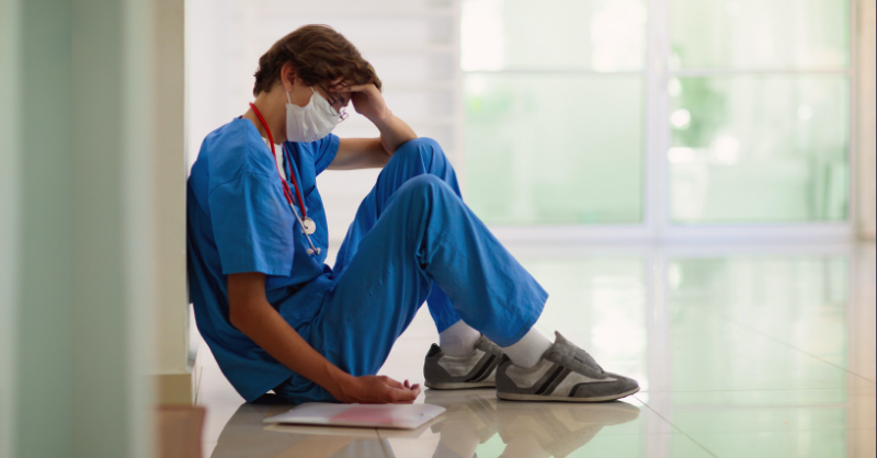 nurse sitting against a wall on the ground looking tired